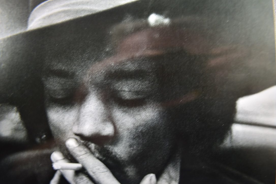 A man smoking a cigarette in front of a picture.