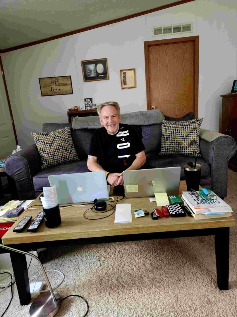 A man sitting on top of a couch in front of two laptops.