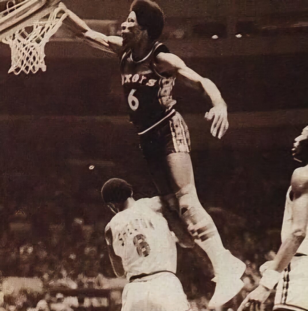 Basketball player dunking over opponent.